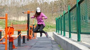 A young female model wearing sportswear is jumping in the air at a park's sports area. The photo is captured with a high shutter speed.